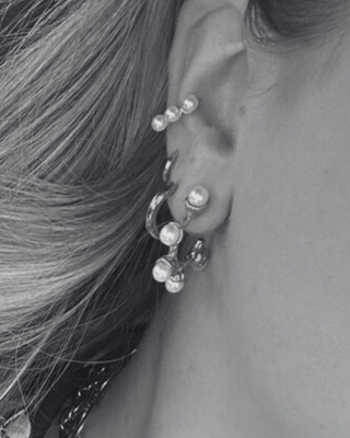 Close-up of an ear with pearl earrings and a necklace, hair flowing in the background