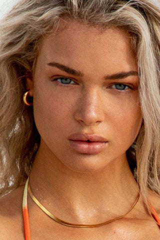 Woman with blonde hair wearing an orange bikini top against a light background