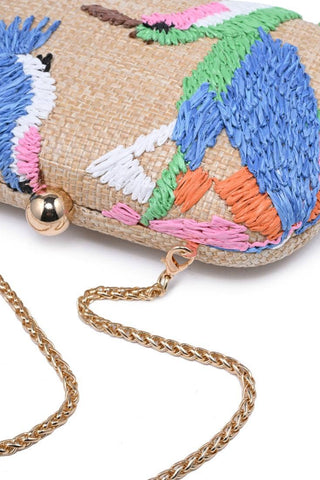 Colorful woven clutch with embroidered parrot design and gold chain strap on a white background