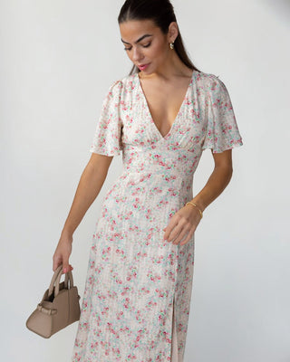 Woman wearing a floral dress holding a handbag against a plain background