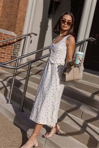 Woman in a floral dress standing on steps holding a coffee cup.