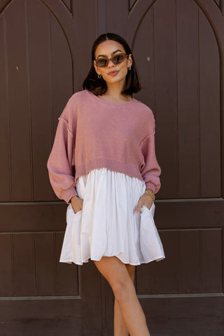 Woman wearing a pink sweater over a white dress against a brown background