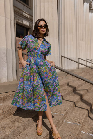 Woman in a floral dress standing on a stone pavement with classical architecture in the background