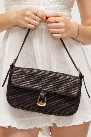 Chocolate woven handbag held by a person wearing a white dress.